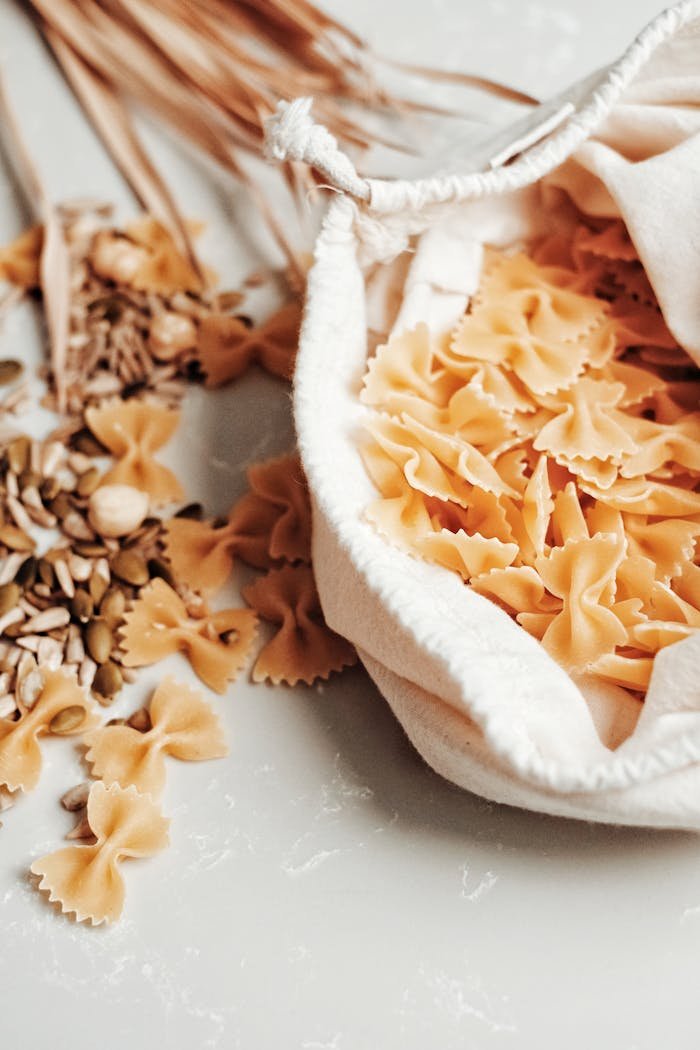 Close-up of farfalle pasta and seeds in a reusable bag, promoting sustainability.
