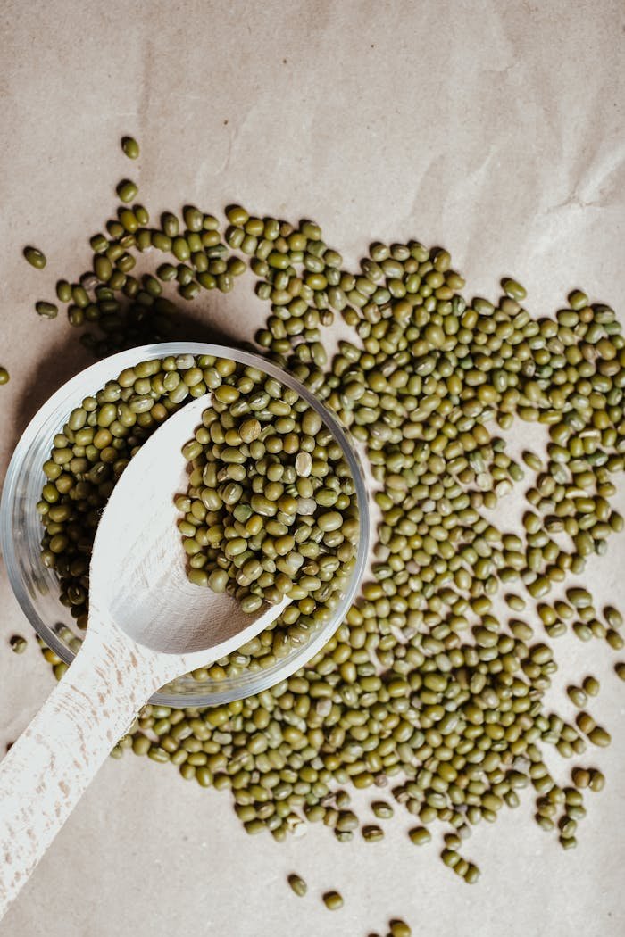 A top view of mung beans spread with a wooden spoon against a neutral backdrop.